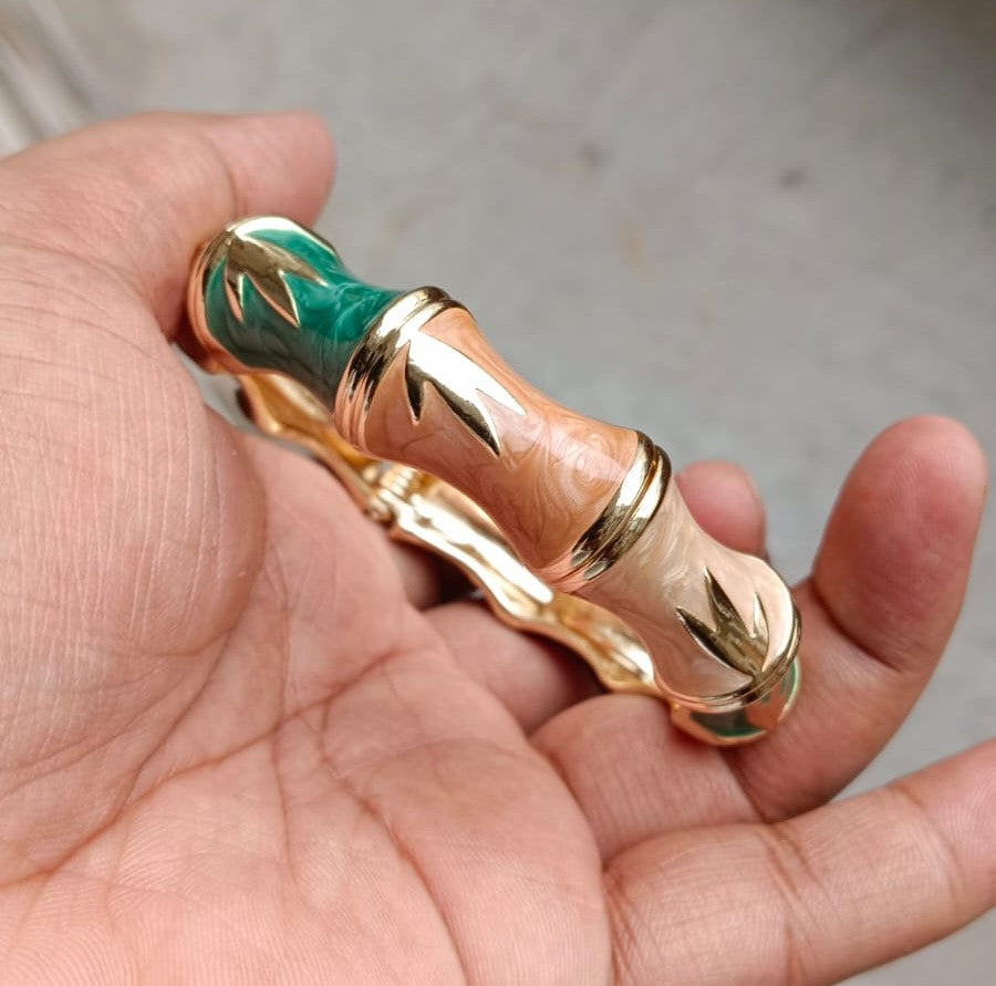 Side view of NAXAYA Bamboo Muse bangle standing upright, showing multicolour enamel segments and golden leaf motifs.