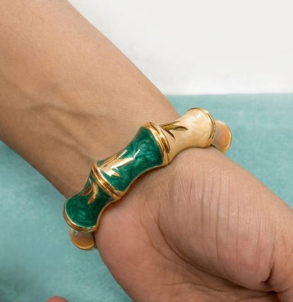 NAXAYA Bamboo Muse bangle worn on a wrist, showing pink, cream, brown and green enamel with gold-tone leaf details.