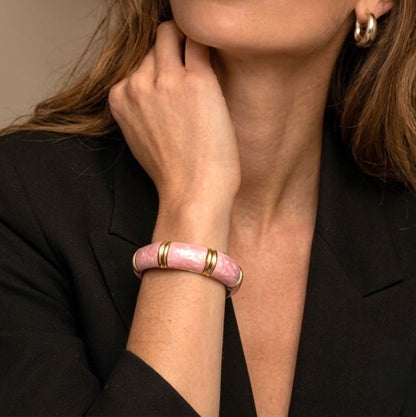  NAXAYA Aura Pink enamel bangle with marble-effect swirls and gold-tone ridges on a model's wrist.

