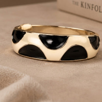 NAXAYA Modern Noir kada bracelet beside a book, showing black half-moon enamel on a gold-tone band.