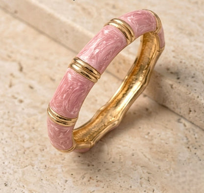 NAXAYA Aura Pink bangle displayed at an angle on beige stone, showing pink marble-effect enamel and golden ridges.