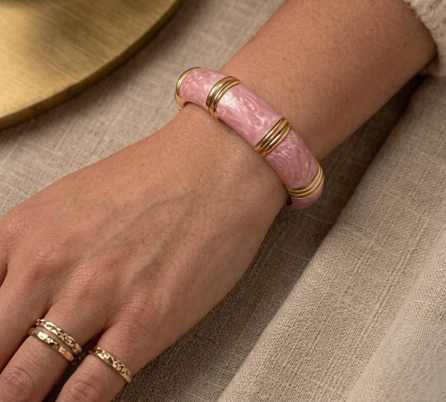 NAXAYA Aura Pink marble-effect enamel bangle styled on a wrist with gold-tone rings and a cream sleeve.