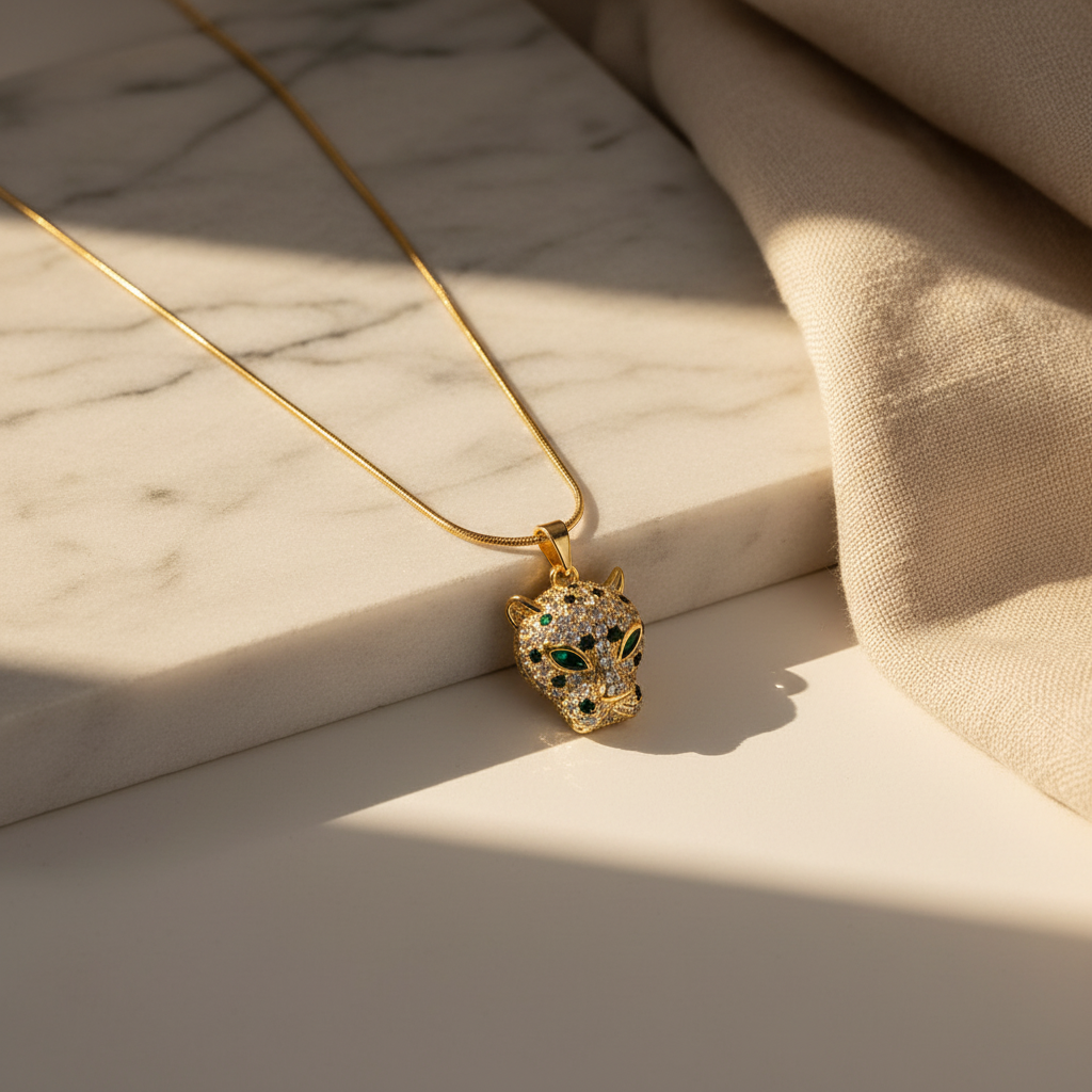 NAXAYA panther pendant with green eyes and clear stones on a gold-tone chain, resting at the edge of white marble.