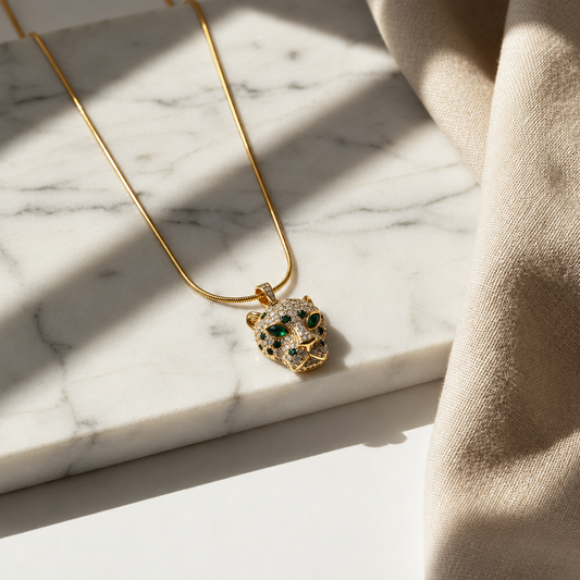 NAXAYA gold-tone panther pendant necklace with green eyes, clear stones and black accents on white marble.